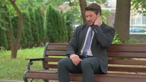 Mature Adult Businessman Experiencing Neck Pain in the Park