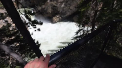 Mulher estendendo a mão em direção à cerca olhando para as Cataratas Sunwapta no Parque Nacional Jasper