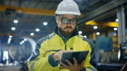 Industrial Engineer in Hard Hat Wearing Safety Jacket Uses Touchscreen Tablet Computer. He Works at