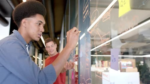 Brainstorming criativo masculino birracial com diversos colegas fazendo anotações na parede de vidro, câmera lenta