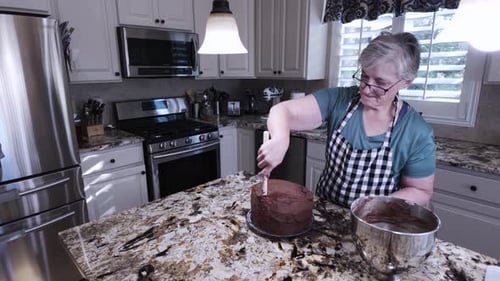 Woman Frosting Chocolate Cake in Kitchen