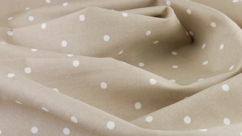 Top view of the soft folds of light beige with white polka dots cotton fabric rotated