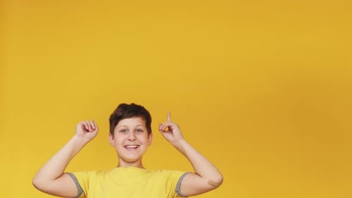 Cheerful Boy Pointing Upward on Yellow Background