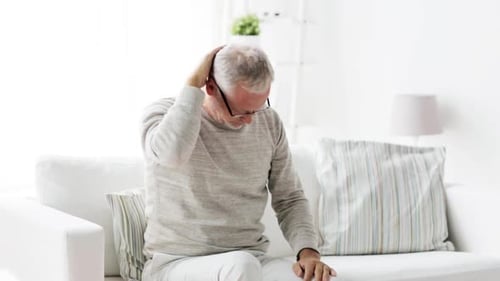 Senior man neck pain massage while sitting at home
