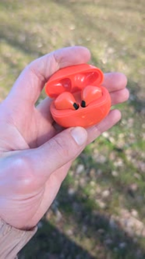 Hand Holding Wireless Ear Buds in an Orange Case