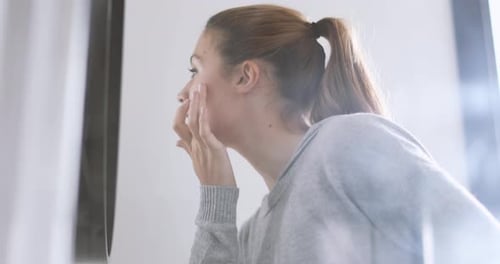 Young adult female looking in mirror examining skin