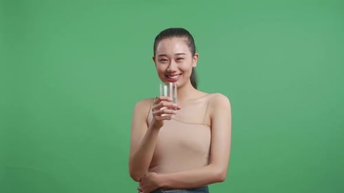 Asiatische Frau trinkt Wasser, während sie auf Greenscreen-Hintergrund im Studio steht