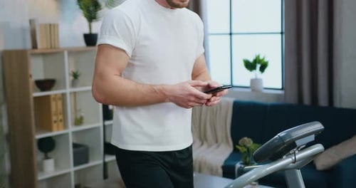 Close up of hands man uses smartphone during morning home workout on running track while stepping