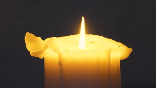 Slow moving close up shot around a lit candle in a dark room.