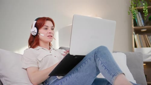 Young Woman Works Using an Internet Headset and a Laptop Communicates Via Video Communication While