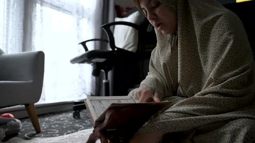 Young Indian female Muslim siting cross legged quietly reading Holy Quran at home