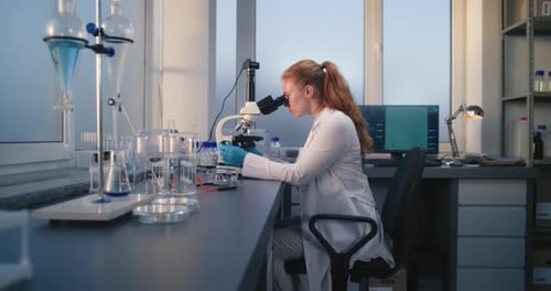 Female Scientist Examining Sample Under Microscope in Lab