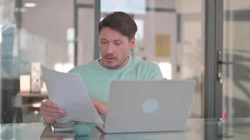 Man Working on Laptop Reviewing Documents
