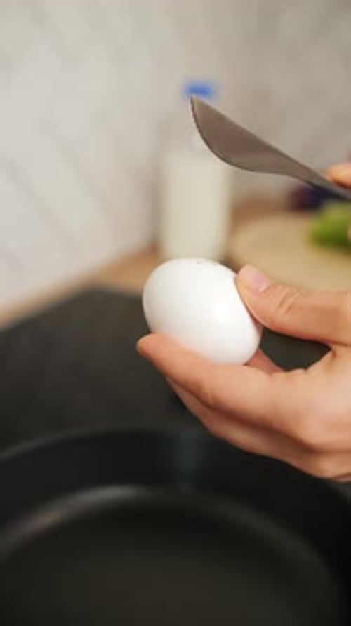 Female Hands Breaking an Egg Over a Frying Pan with a Knife Close Up