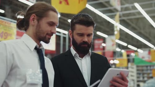 Handsome Seller Consultant Talk with Young Beard Man Use Hold Touch Tablet Computer in Tech Store