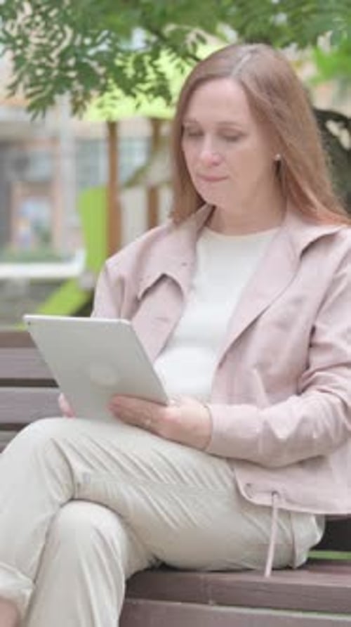 Woman Using Tablet Device on Bench in Urban Setting