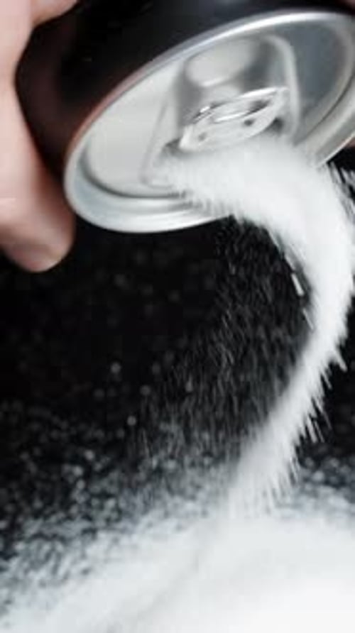 Vertical video. Pure white sugar being poured from a soda can onto a black table by a man.