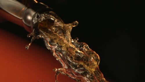 Close Up Of Beer Pouring Down From A Glass Bottle In Slow Motion On Terracotta Background