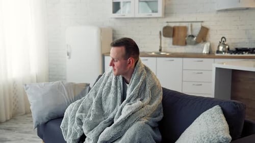 Man Wrapped in Blanket Resting on Sofa