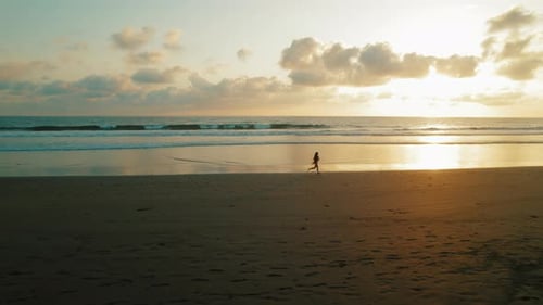 Woman jogging on sandy beach at sunset with calm ocean waves