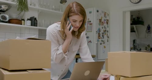 Woman Talks on Phone With Laptop and Shipping Boxes