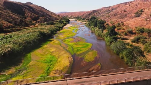 Aerial View Moving Towards a Bridge Over a River with Lush Green Vegetation on Its Banks Surrounded