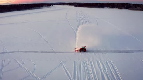 Red Tractor with a Snowplow Clearing a Path on a Frozen Lake