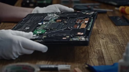 Hands Repairing Disassembled Laptop on Wooden Desk