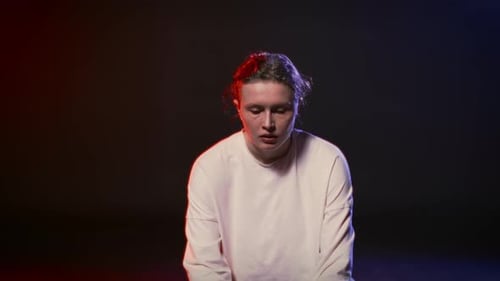 Woman Sits in Dark Room with Red and Blue Lights