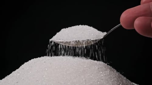 Einen Löffel voll Zucker aus einem Zuckerhaufen auf schwarzem Hintergrund in Zeitlupe
