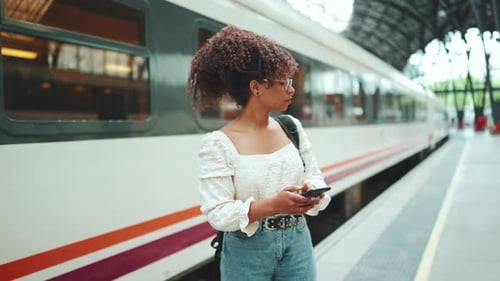 Frau mit Smartphone geht den Bahnsteig neben dem Zug entlang und schaut sich um