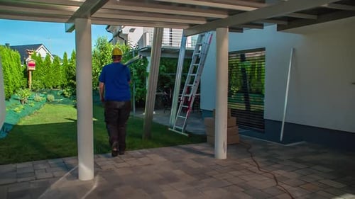 Telhado carregando trilhos de painel solar no ombro para serem colocados ao lado da escada. Câmera lenta, câmera de rastreamento
