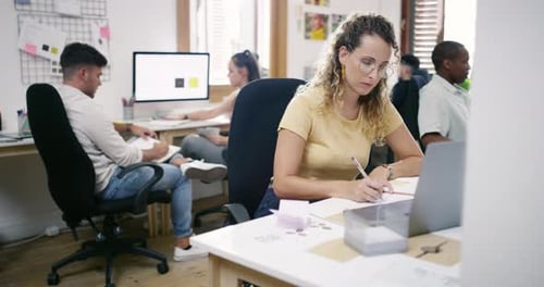 4k video footage of a young businesswoman using a laptop and making notes in a modern office