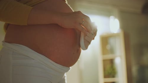 Pregnant Woman Holds Baby Shoes to Her Belly