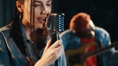 Zwei multiethnische Freunde üben gemeinsam im Studio Gesang. Mädchen singt, Typ spielt Gitarre