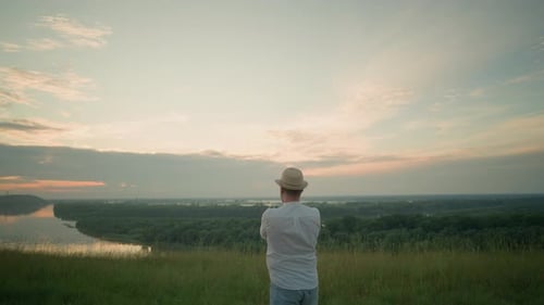Thoughtful Man Gazing Over a Tranquil Lake at Sunset in a Grassy Field