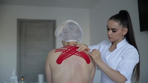 Woman Applying Kinesiology Tape to Patient's Back