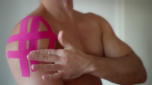 Man Examining Pink Medical Tape on Shoulder