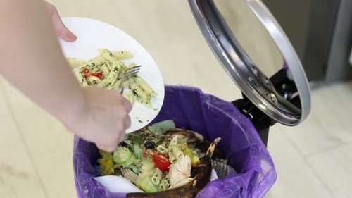 Mujer tirando desperdicios de comida a la basura en la cocina, primer plano