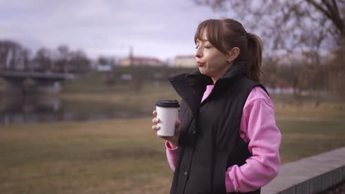 Young woman enjoying coffee and smartphone by the river