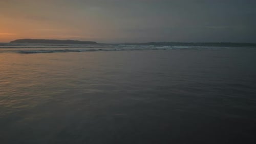 Seascape view of ocean waves crashing on the shoreline, at sunset, on a cloudy evening