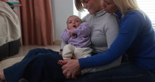 Happy female gay couple having tender moment with their baby son at home