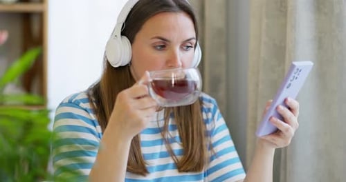 Woman Drink a Cup of Tea and Listening to Music with Headphones in the Lounge