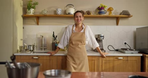 Portrait of a Happy Baker Girl in a White Shirt and Beige Apron Posing in the Kitchen in a Bakery