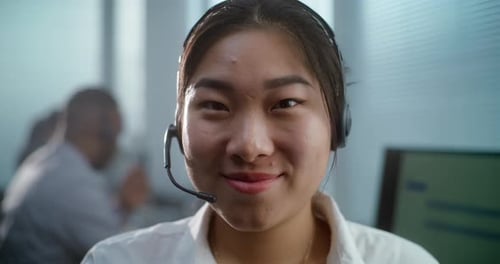 Female Hotline Operator in Headset Smiles and Looks at Camera