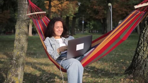 Female Freelancer Lying in a Hammock in the Park Using a Laptop Work in the Fresh Air