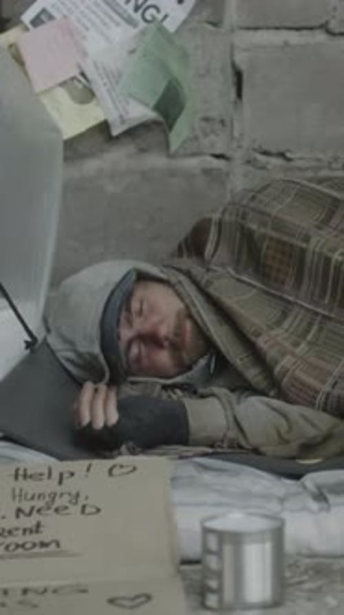 Vertical of Troubled Young Man Sleeping on Ground Bundled in Plaid Blanket