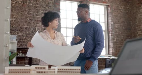 Diverse architect colleagues discussing work with building model and blueprints in slow motion