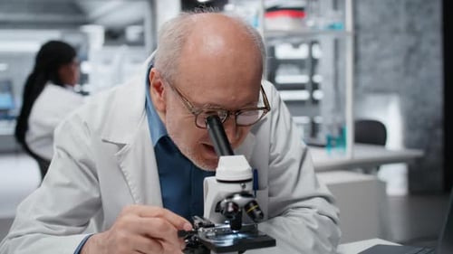 Senior scientist looking through microscope in lab