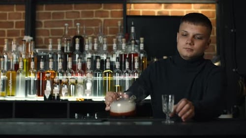 Close up of bartender at a bar counter pouring alcohol into vintage glass. Media. Pouring red hot